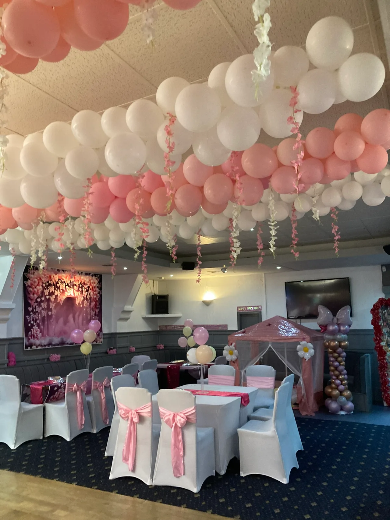Tables and chairs beneath pink and white balloons at a party